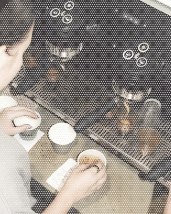 Overhead view of a cafe counter, a barista's hands wiping a cup beside the espresso machine's drip trays.