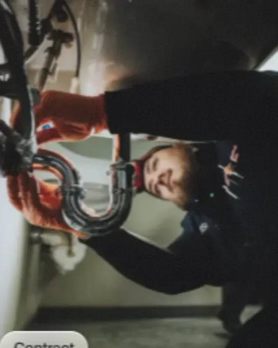 A plumber on his back under a sink, working the trap loose with a wrench.