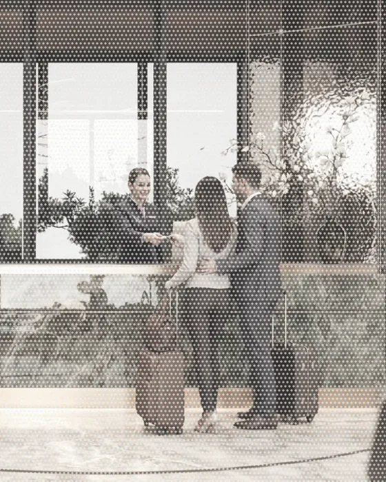 A hotel receptionist greeting a guest with a suitcase across the front desk.