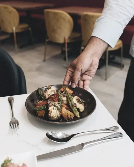 A cook's hand setting down a plate of asparagus at a laid restaurant table, cutlery beside it.