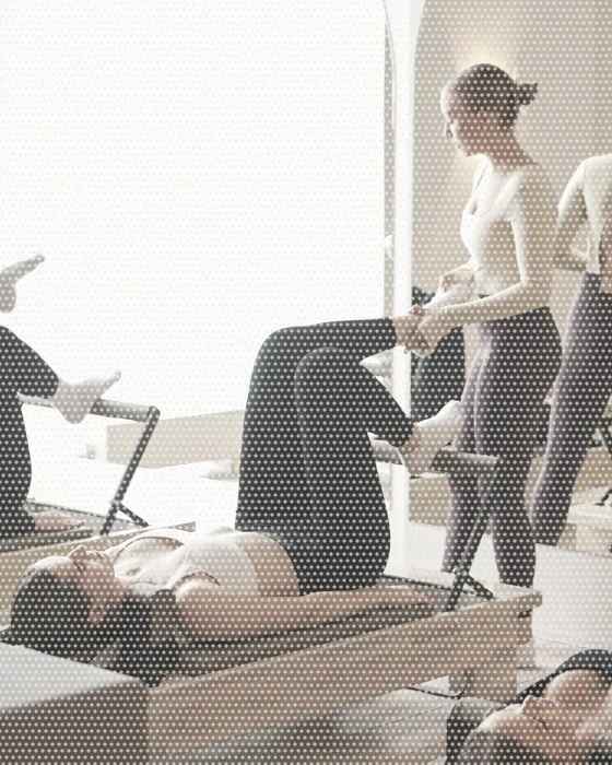 An instructor guiding clients through a class on reformer beds in a bright pilates studio.
