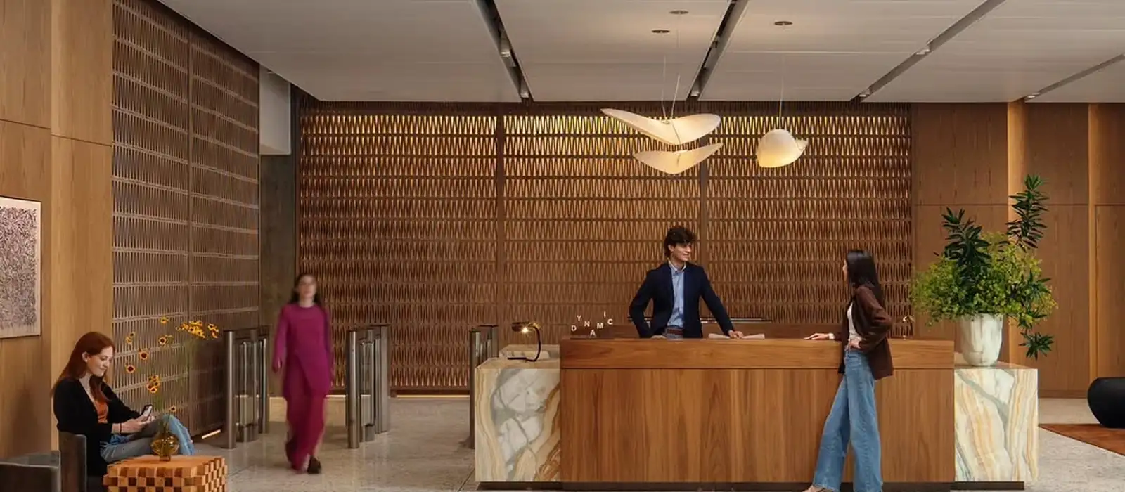 A hotel receptionist behind a long wooden desk speaking with a guest, two more guests crossing the lobby behind them.