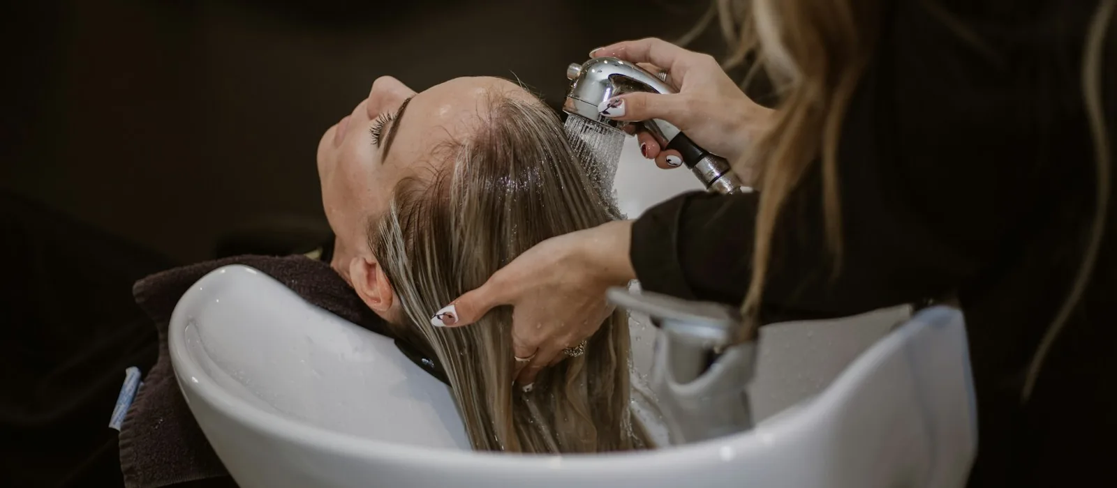 A stylist rinsing a client’s hair at the salon basin, both hands occupied.